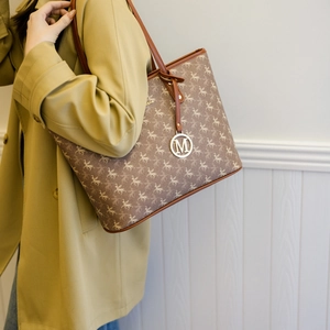 Sac cabas marron à imprimé Pégase et logo doré porté à l'épaule sous une lumière douce