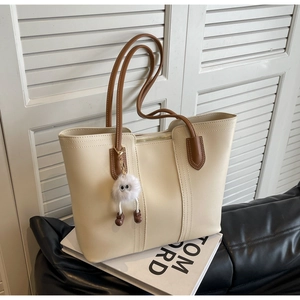 Detailed view of cream PU leather tote bag with brown straps and plush ball charm accessory