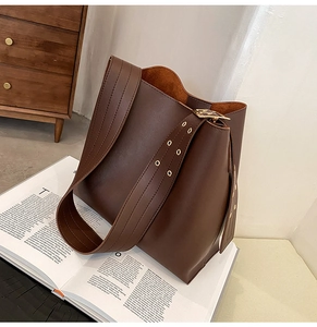 Détail du sac seau en cuir marron montrant la bandoulière large et la boucle dorée