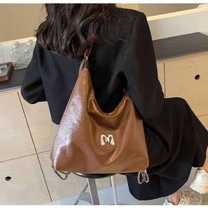Detail of a large brown hobo bag with a silver M logo and decorative metal chains