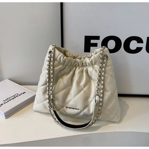Detail of quilted leather texture and silver chain on beige bucket bag with drawstring