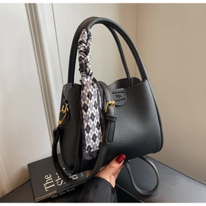 Close-up of black lychee leather bucket bag with gold hardware and checkered scarf detail