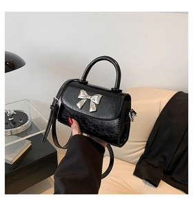 Detail of black pleated PU leather handbag with silver metallic bow and curved handle
