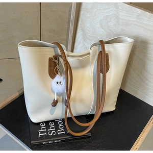 Close-up of cream tote bag with brown handles, stitching, and cute plush ball charm