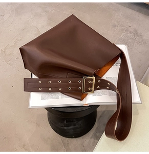 Détail d'un sac seau en cuir marron foncé avec large bandoulière à œillets sur livre