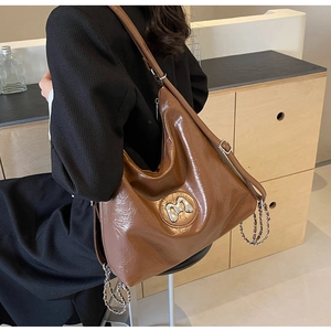 Detail of vintage brown leather tote bag featuring metal M logo and chain decoration