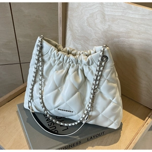 Macro shot of white quilted drawstring bag with silver chain strap on a business book
