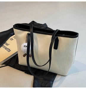 Detail of a large cream tote bag with black straps and a cute plush ball keychain