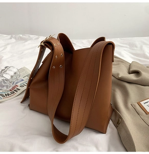 Détail de la large bandoulière avec boucle triangle dorée sur le sac seau en cuir brun