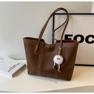 Detail of brown tote bag with white contrast stitching and cute plush ball charm