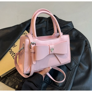 Detail of pink bow handbag featuring a silver heart buckle and pebbled leather texture