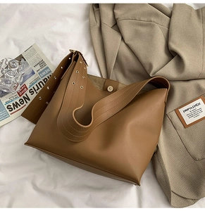 Détail du sac seau marron en cuir avec rivets dorés sur bandoulière large et fermoir aimanté