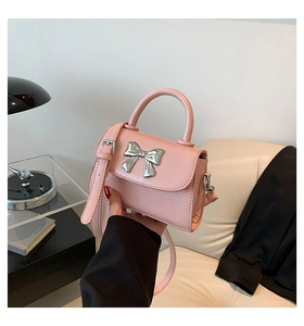 Detail view of pink crossbody bag with silver bow ornament and leather texture