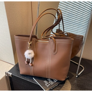 Detail of brown tote bag with white contrast stitching and soft plush ball charm