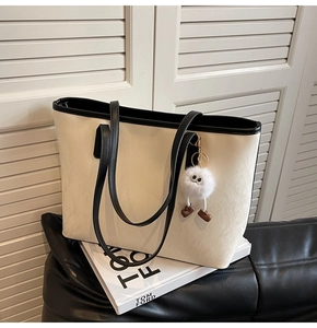 Detail of off-white tote bag with black contrast trim and a cute plush doll charm