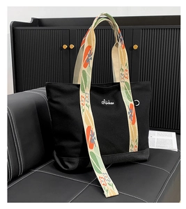 Détail du cabas en toile noire avec bandoulière fleurie et broderie de marque