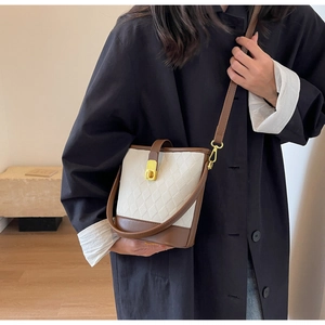 Détail du sac seau matelassé beige avec garniture en cuir brun et fermoir doré
