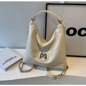 Detail of cream large tote bag with metallic M ornament and shiny leather texture