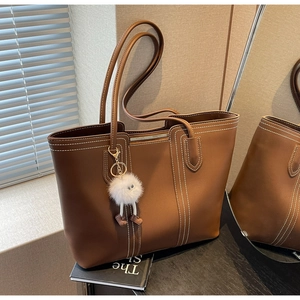 Detail of brown tote bag with white double stitching, metal zipper and plush charm