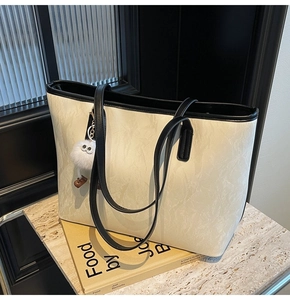 Detail of off-white tote bag with black piping and plush eye charm on a display table