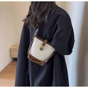 Détail du sac seau matelassé beige avec bordure en cuir marron et fermoir doré