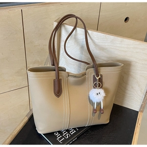 Detail of light brown tote bag featuring contrast stitching and plush monster charm