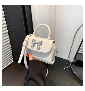 Detail of white mini crossbody bag featuring a metallic silver bow buckle and handle