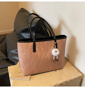 Detailed view of pink tote bag with crinkled texture and white plush charm on stone base