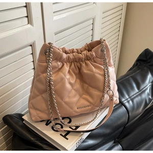 Detailed view of pink quilted bucket bag with chain strap on a black leather sofa