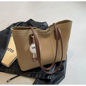 Detail of khaki tote bag with white stitching and plush monster charm on leather jacket