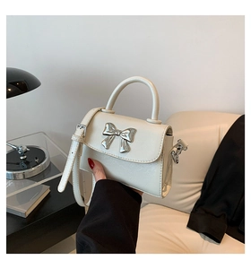 Detail of a creamy white leather handbag with a metallic silver bow buckle and strap
