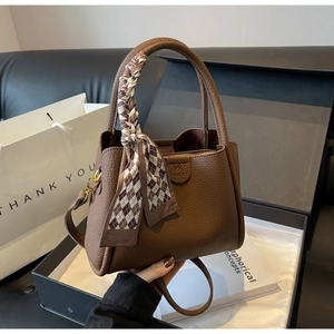 Close-up of brown litchi leather bucket bag with decorative plaid scarf and top handle