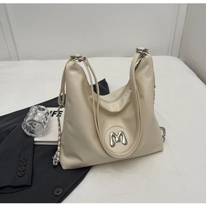Close-up of cream textured leather tote bag featuring a silver metal M logo and chain strap