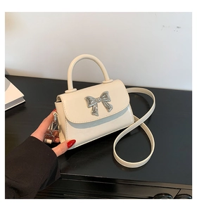 Detail of a beige crossbody bag featuring a silver metal bow and detachable shoulder strap