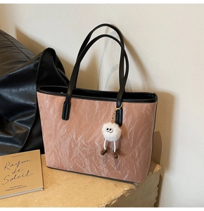 Detail of rose gold ripple textured tote bag with cute white fluffy charm on stone surface