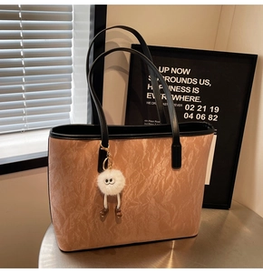 Detail of light brown tote bag with textured faux leather, black trim and white plush charm
