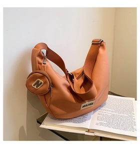Détail d'un sac demi-lune orange posé sur un livre avec une petite pochette ronde