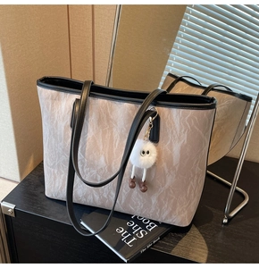 Detail of light grey pleated tote bag with black straps and cute white plush ball charm