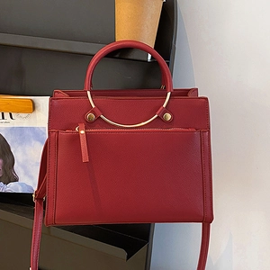 Deep red leather bridal handbag with golden metal handles and adjustable strap on a stand