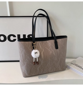 Detail of khaki tote bag with black trim and a white plush monster pendant detail