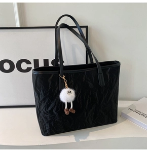 Close-up of black pleated tote bag with plush eye charm and durable leather straps