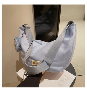 Détail du sac hobo bleu clair avec large bandoulière et mini pochette sur livre