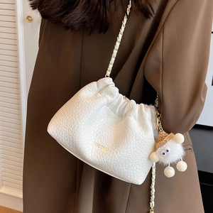 White textured chain shoulder bag with plush charm and gold branding on blazer