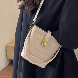 Sac seau matelassé beige avec fermoir doré porté sur un manteau noir élégant et moderne