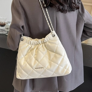 Beige quilted leather bucket bag with silver chain strap worn by a model in gray suit