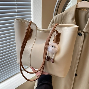 Large cream tote bag with brown straps and plush charm, stylish urban commuter style