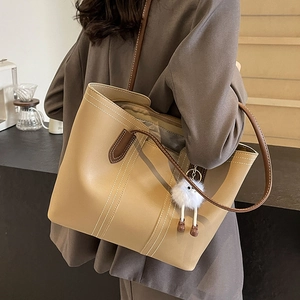 Large khaki tote bag with contrast stitching and plush doll on a stylish shoulder strap