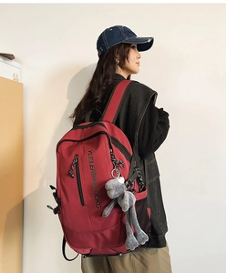 Side view of large burgundy school backpack featuring a grey plush bunny pendant on model