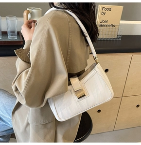 Detail of cream white underarm bag featuring wave texture and golden buckle on wooden table
