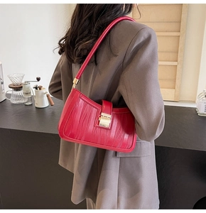 Macro detail of red embossed leather handbag with gold clasp on a minimalist counter
